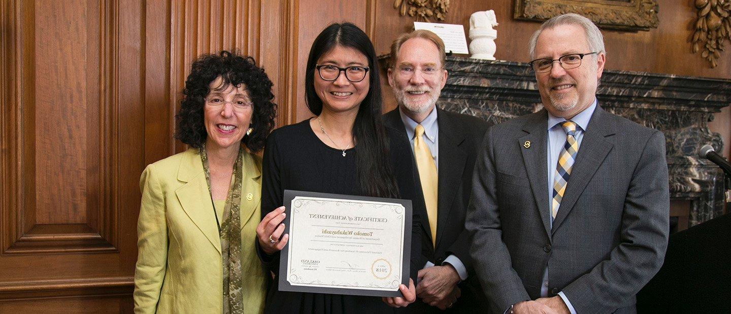 Four people posing for a group photo. One woman is holding a certificate.